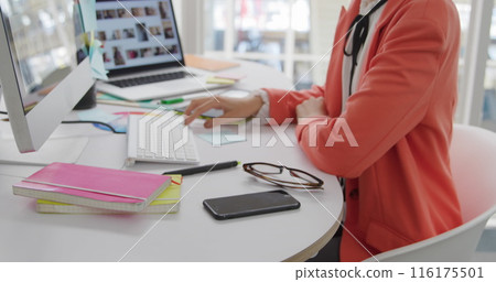 Image of asian colleague wearing bright orange blazer, using a computer Image of asian colleague wearing bright orange blazer, using a computer 116175501