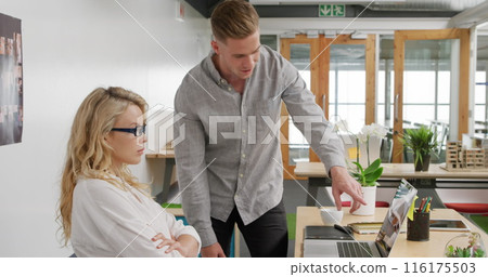 Image of caucasian colleague pointing at laptop screen, female wearing glasses watching 116175503