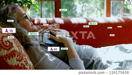 Image of social media icons over caucasian senior woman with a book lying on the couch at home 116175638