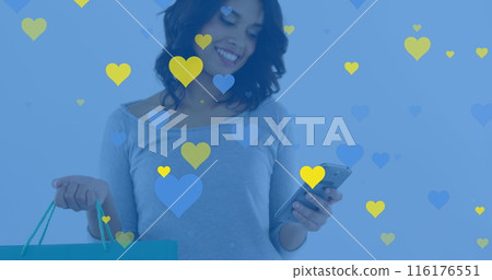 A young woman with dark hair is holding shopping bag and looking at her smartphone 116176551