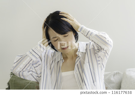 Middle-aged woman sitting on sofa holding her head, headache 116177638