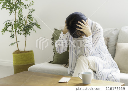 Middle-aged woman sitting on sofa holding her head, headache Middle-aged woman sitting on sofa holding her head, headache 116177639