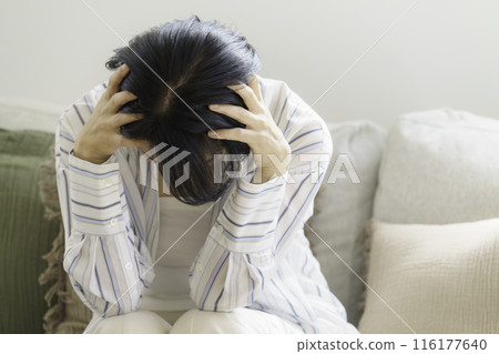 Middle-aged woman sitting on sofa holding her head, headache Middle-aged woman sitting on sofa holding her head, headache 116177640