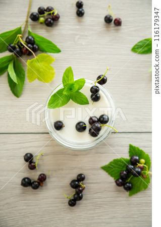 homemade sweet yogurt in a jar with black currants, on a wooden table homemade sweet yogurt in a jar with black currants, on a wooden table 116179347