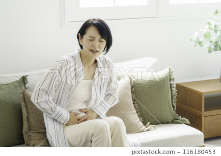 中年婦女坐在沙發上摀著肚子，腹痛 116180453