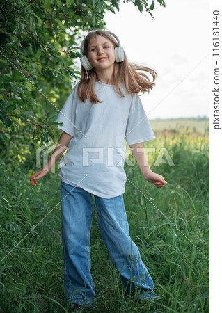 A child with headphones listening to music and dancing in the park. A child with headphones listening to music and dancing in the park. 116181440