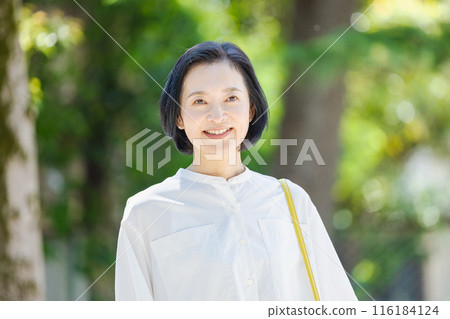 Middle-aged woman walking in the fresh greenery Middle-aged woman walking in the fresh greenery 116184124