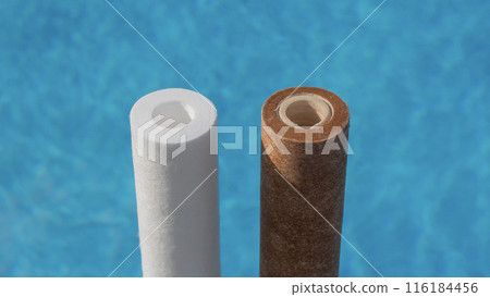 Two water filter cartridges, one clean and one dirty, beside a swimming pool. 116184456