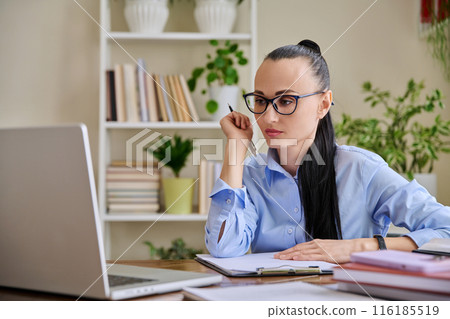 Business woman with clipboard sitting at workplace, looking talking at computer screen Business woman with clipboard sitting at workplace, looking talking at computer screen 116185519