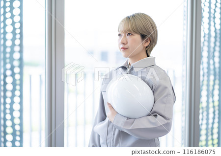 A young woman with short blonde hair wearing work clothes and holding a helmet (free hair color, working in your own way, work environment) 116186075