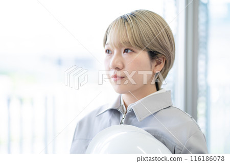 A young woman with short blonde hair wearing work clothes and holding a helmet (free hair color, working in your own way, work environment) 116186078