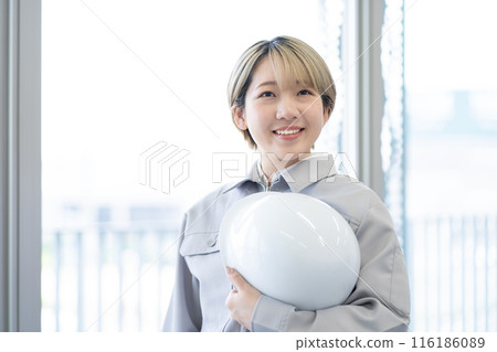 A young woman with short blonde hair wearing work clothes and holding a helmet (free hair color, working in your own way, work environment) 116186089