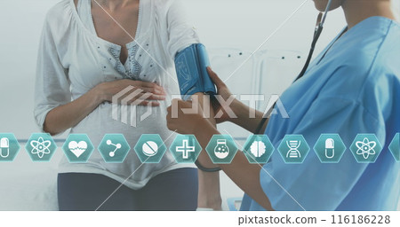 Biracial midwife in blue scrubs checks blood pressure of Caucasian midwife 116186228