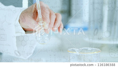Caucasian senior male scientist holding flask, examining a clear liquid 116186388