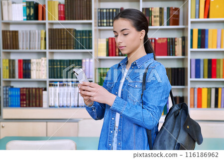 Teenage female student using smartphone, inside high school building, in library Teenage female student using smartphone, inside high school building, in library 116186962