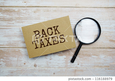 Back Taxes text message and magnifying glass with space copy on wooden background 116188979