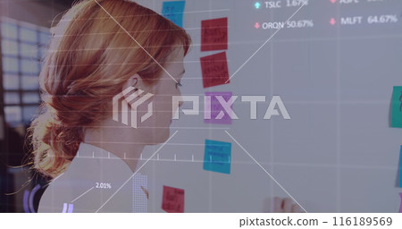 Caucasian woman in her early thirties looking at colorful sticky notes on whiteboard 116189569