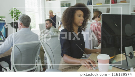 African American woman working on computer in busy office with diverse colleagues 116189574