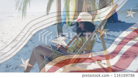 Multiple stars on blue stripes against woman using laptop sitting on deck chair at the beach 116189786