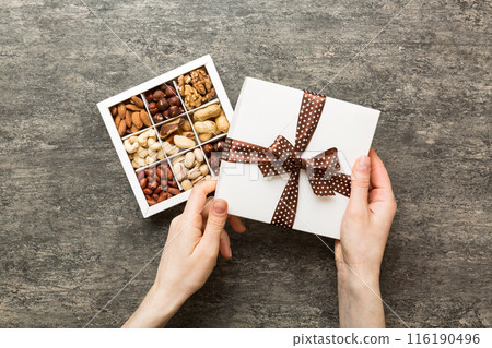 Young woman holding box with different nuts, closeup. Close up, copy space, top view, flat lay. Walnut, pistachios, almonds, hazelnuts and cashews 116190496