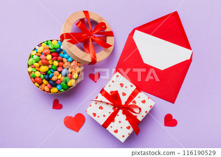 Red envelope with candy and gift box and Valentines hearts on colored background. Flat lay, top view. Romantic love letter for Holiday concept 116190529