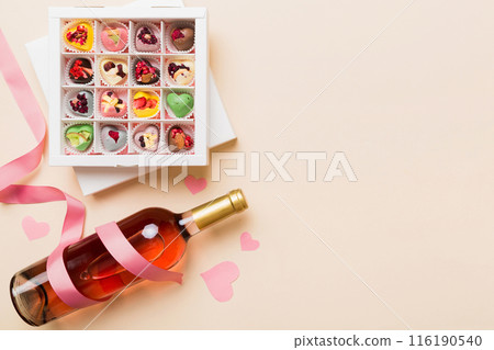 Bottle of red wine on colored background for Valentine Day with gift and chocolate. Heart shaped with gift box of chocolates top view with copy space 116190540