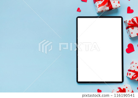Top view of digital tablet with gift boxes and hearts on colorful background. Tablet with black screen with Holiday decorations gift box top view Top view of digital tablet with gift boxes and hearts on colorful background. Tablet with black screen with Holiday decorations gift box top view 116190541