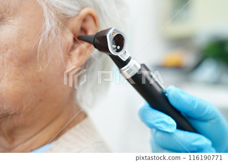 Audiologist use otoscope checking ear of elderly woman patient treating hearing loss problem. 116190771