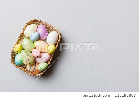Colorful Easter eggs in wicker basket against colored background, closeup. top view with copy space 116190868