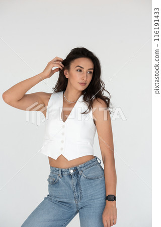 Happy beautiful girl posing in a new hot summer look. Wearing blue jeans and white waistcoat Happy beautiful girl posing in a new hot summer look. Wearing blue jeans and white waistcoat 116191433