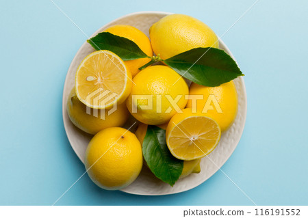 Fresh cutted lemon and whole lemons over round plate on colored background. Food and drink ingredients preparing. healthy eating theme top view vith copy space Fresh cutted lemon and whole lemons over round plate on colored background. Food and drink ingredients preparing. healthy eating theme top view vith copy space 116191552