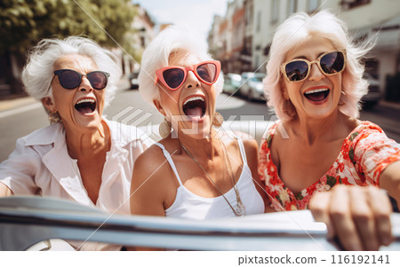 Company of three elderly girlfriends of pensioners ride a cabrio car together and have fun 116192141