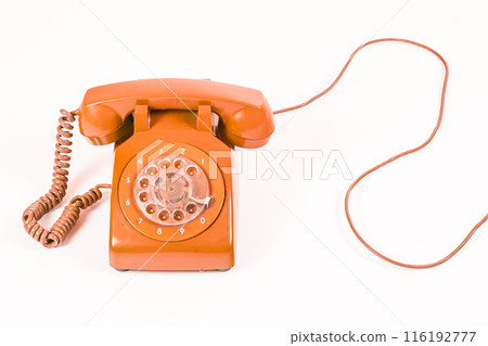 Vintage orange rotary dial telephone with a coiled cord, on a white background, studio shot. 116192777