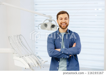 Confident male patient of stomatology standing in modern clinic. Man smiling at the camera crossing his arms in front of him 116193167