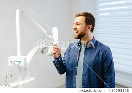 Handsome male patient looking at his beautiful smile standing at the dental office 116193168