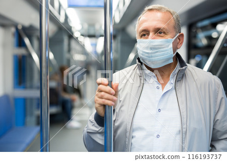 Mature passenger wearing protective mask rides in an underground metro car 116193737