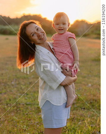Cheerful woman with her infant girl with sunset tones in park. Happy family outdoor Cheerful woman with her infant girl with sunset tones in park. Happy family outdoor 116194200