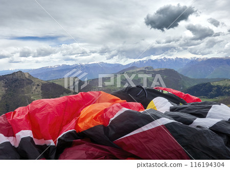 Colorful Paragliders Spread Out on a Mountain Meadow Before the Italian Alps Colorful Paragliders Spread Out on a Mountain Meadow Before the Italian Alps 116194304