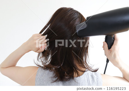 一個女人用吹風機烘乾她的頭髮 一個女人用吹風機烘乾她的頭髮 116195223