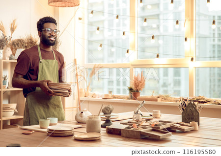 Dark-skinned man in eyeglasses working with pottery in his workshop Dark-skinned man in eyeglasses working with pottery in his workshop 116195580