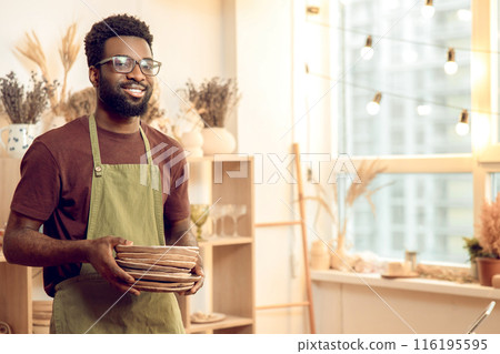 Dark-skinned man in eyeglasses working with pottery in his workshop 116195595