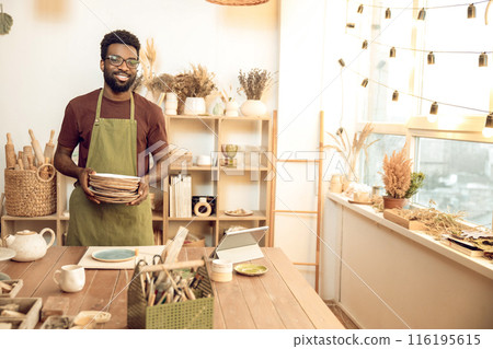 Man in apron standing with ceramic plates in hands Man in apron standing with ceramic plates in hands 116195615