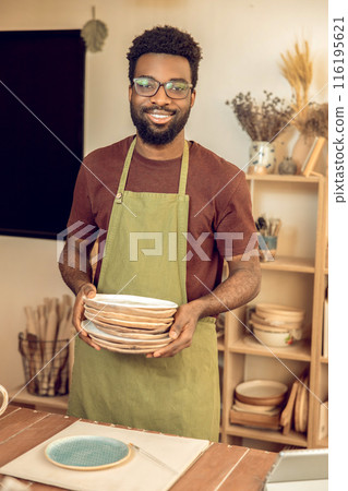 Man in apron standing with ceramic plates in hands Man in apron standing with ceramic plates in hands 116195621