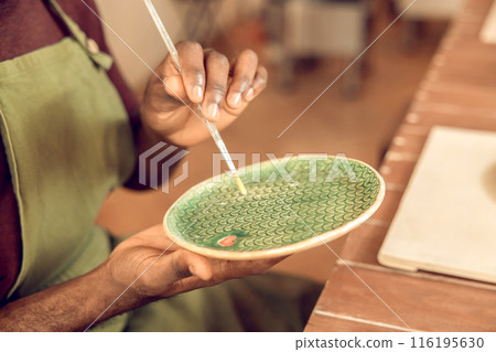 Close up of mans hand painting the ceramic plate with the brush 116195630