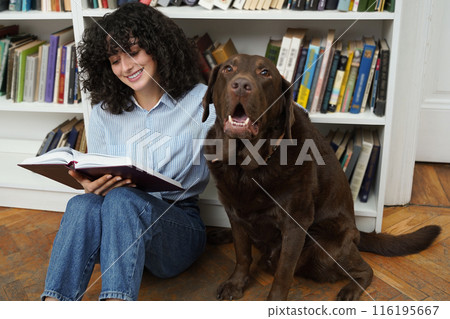 Curly-haired woman sitting on the floor in a library with a dog 116195667