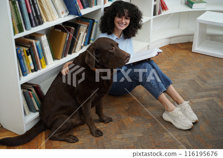 Curly-haired woman sitting on the floor in a library with a dog 116195676
