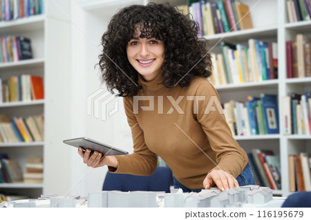 Curly-haired woman working on miniature project in a library Curly-haired woman working on miniature project in a library 116195679