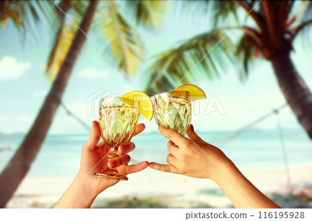Honeymoon romance. People relaxing on beach, holding wine glasses with orange slices. Beautiful tropical background with palms, sea and hammock Honeymoon romance. People relaxing on beach, holding wine glasses with orange slices. Beautiful tropical background with palms, sea and hammock 116195928