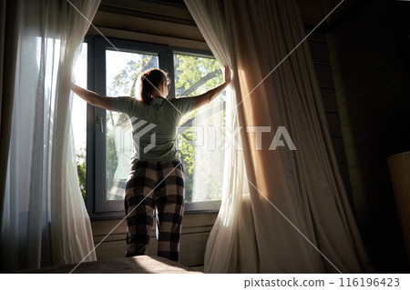 Woman Opening Curtains to Bright Morning Sunlight 116196423