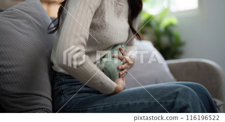 Woman Using Hot Water Bottle for Pain Relief at Home - Healthcare and Wellness Concept 116196522